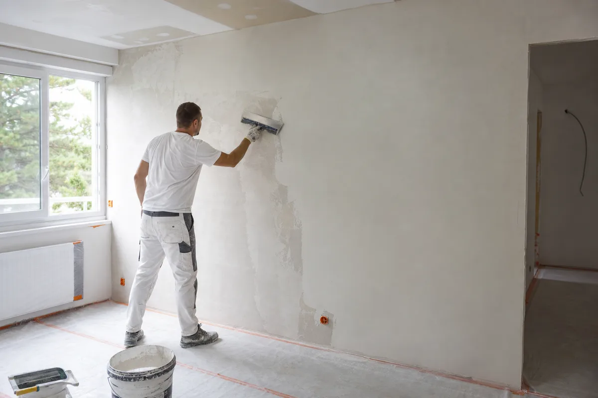 Peintre appliquant un enduit de lissage à la lame sur un mur de séjour